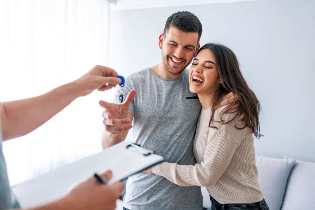 Happy couple is taking keys from their new house from broker and smiling