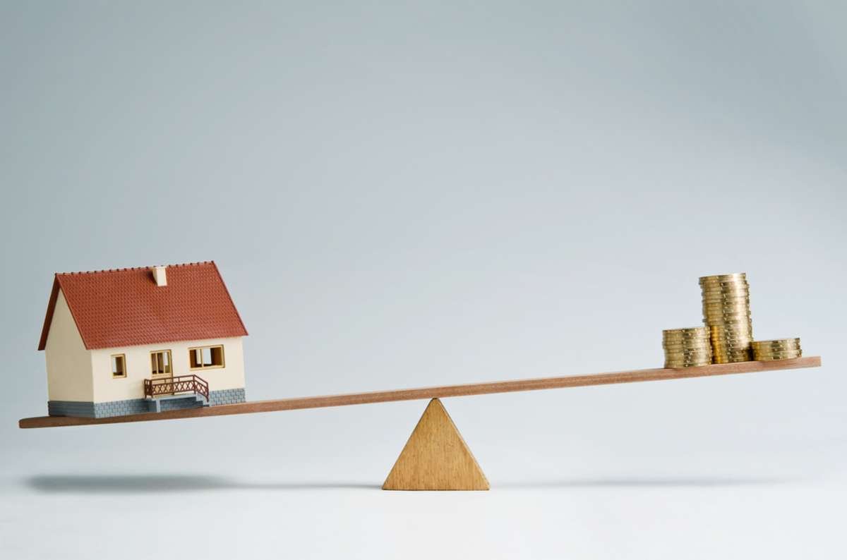 Model house and money coins balancing on a seesaw