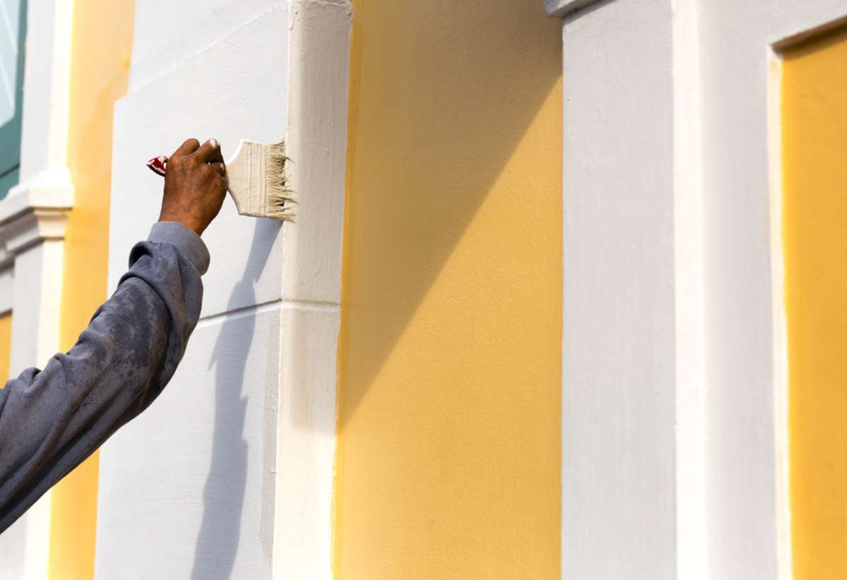 Unidentified man painting with brush on the building wall outside