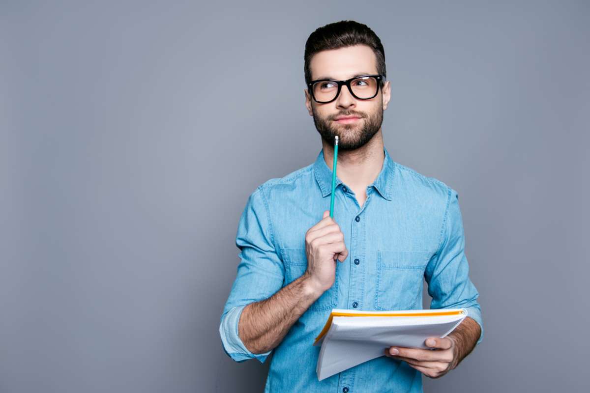 Young bearded guy in glasses holding a notebook and thinking about exams