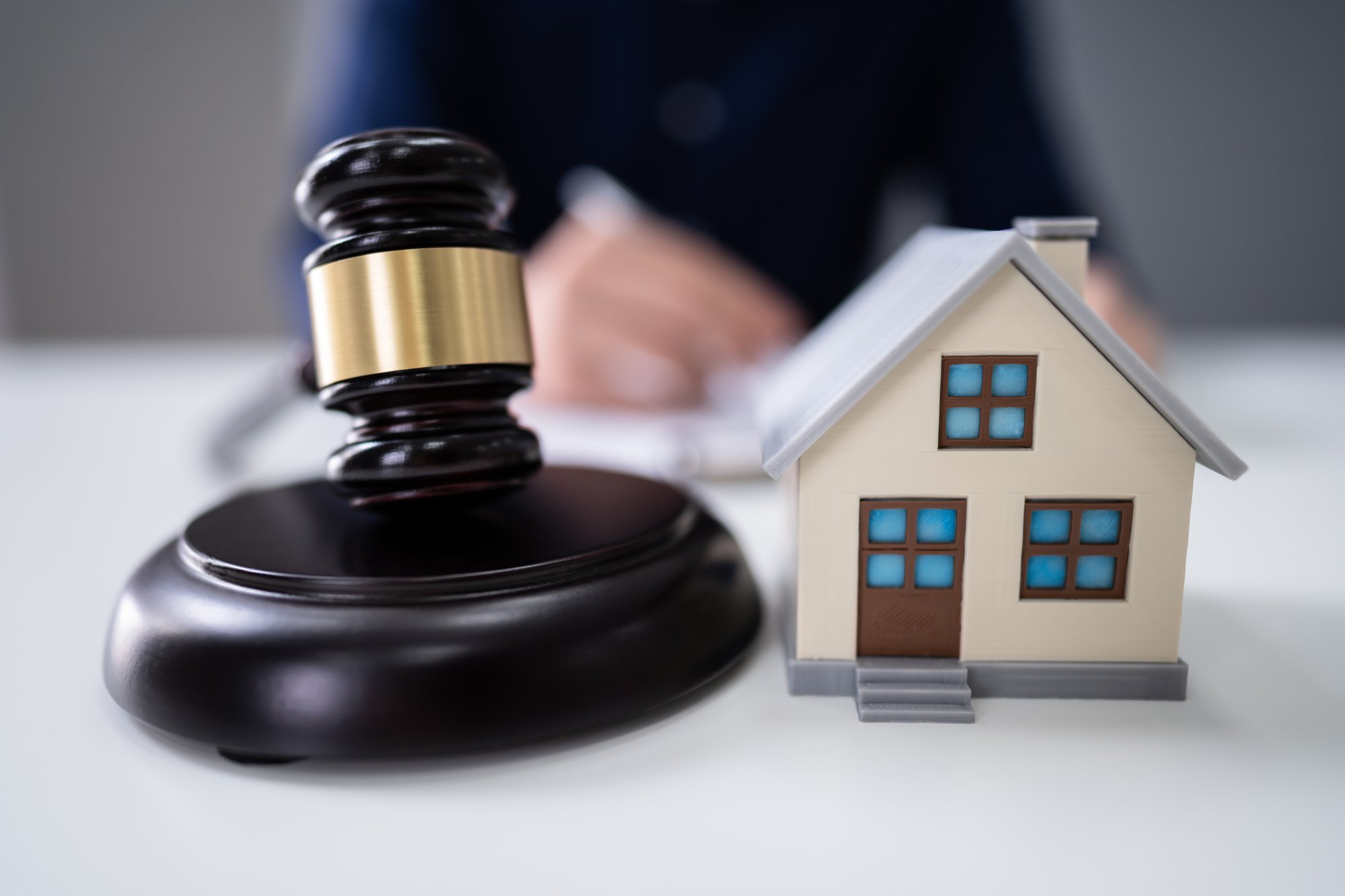 Close-up Of A Judges Hand Striking Gavel Near House Model Over White Table