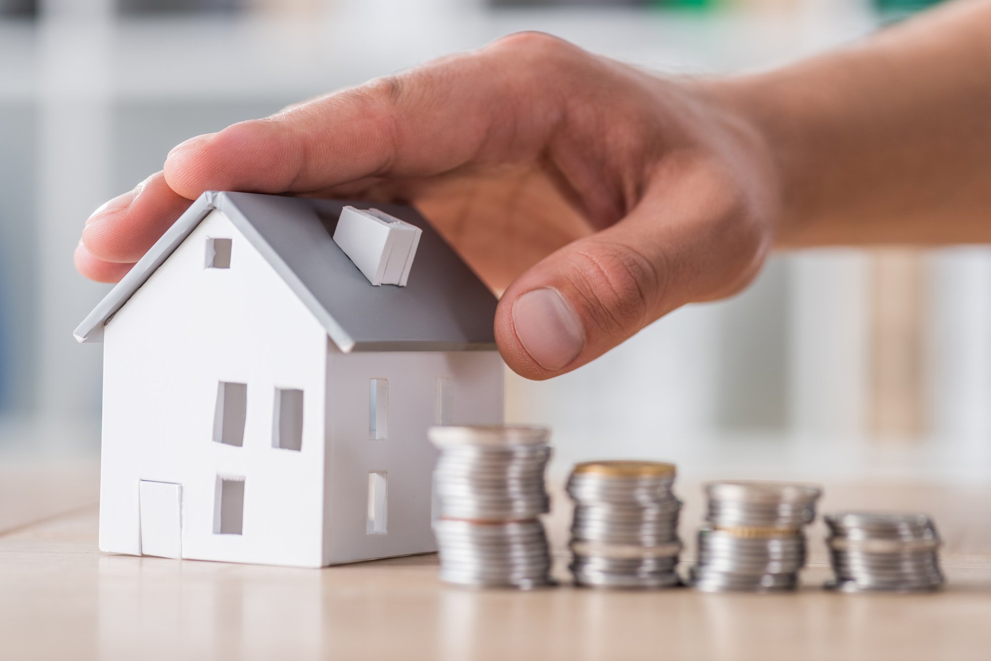 Cropped view of businessman touching roof of house model near stacked coins