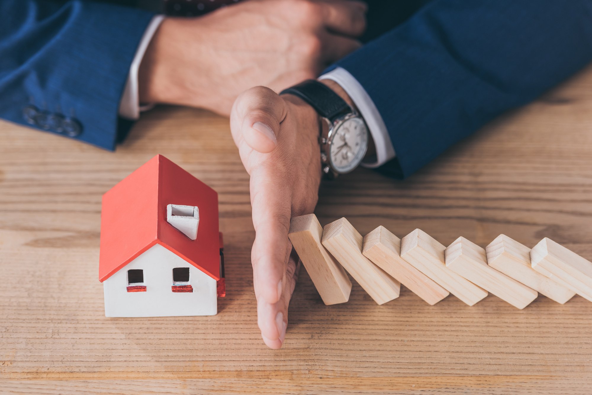 Cropped view of risk manager protecting house model from falling wooden blocks with hand