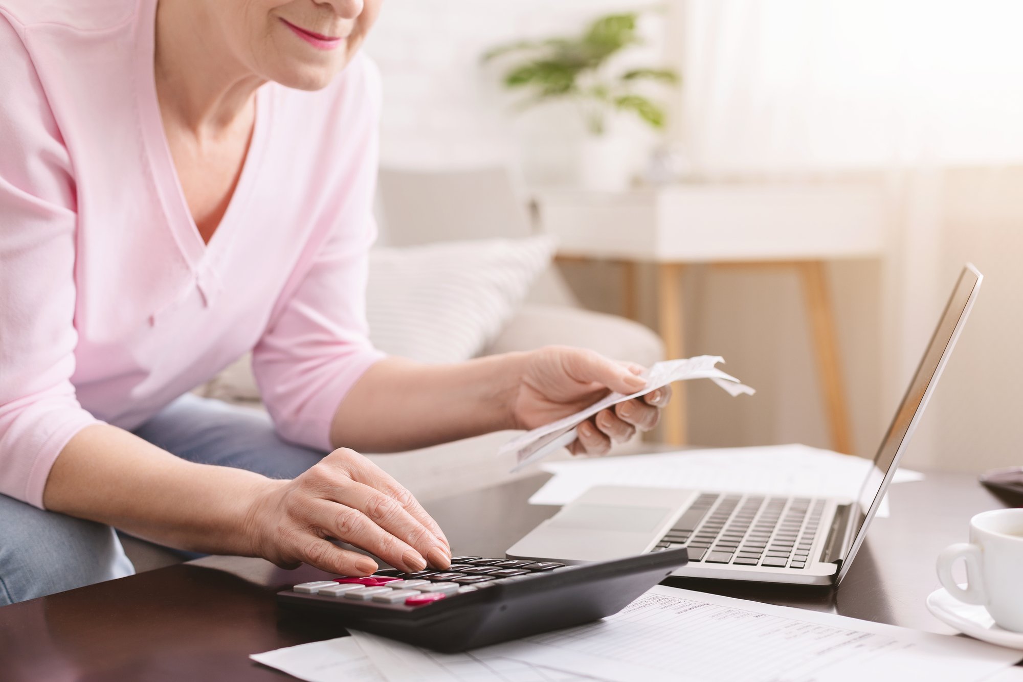 Senior lady counting bills with calculator at hom