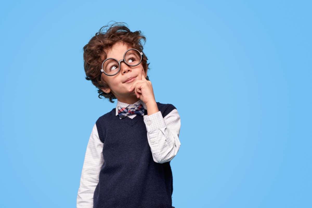 Smart wunderkind in nerdy glasses and school uniform touching cheek and looking up