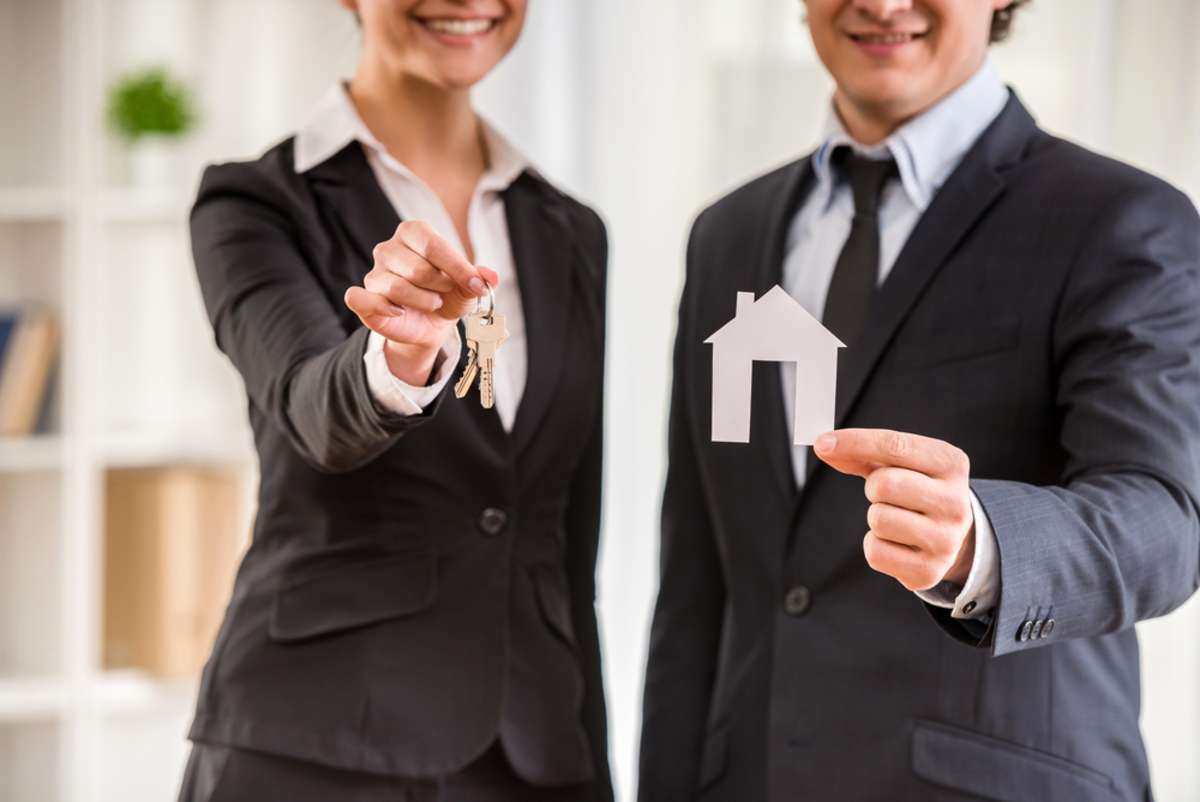 Two realtors in suits are showing a model of house and keys