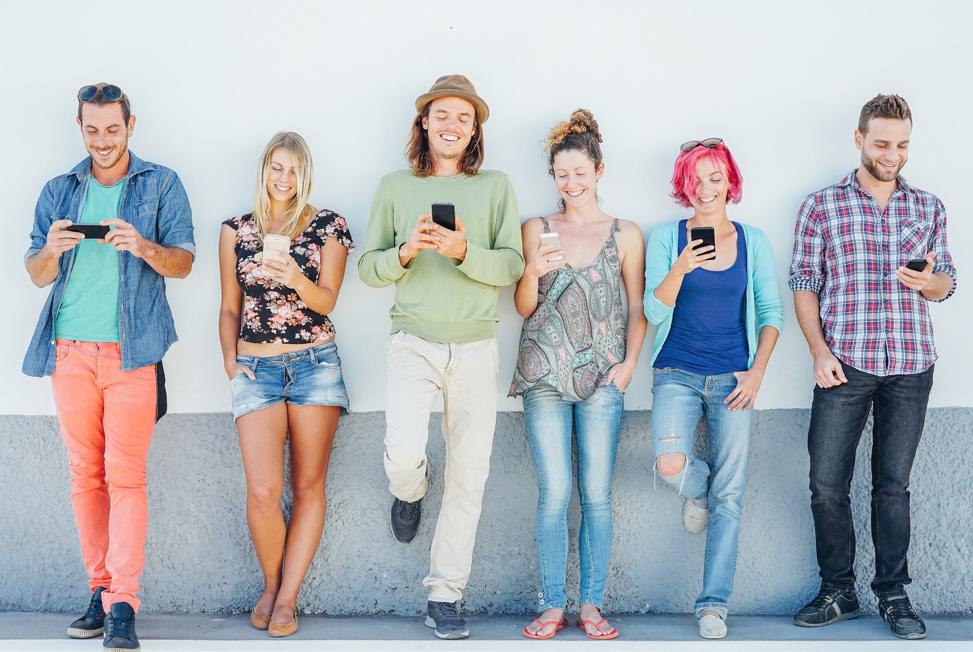 Young people watching on their smart mobile phones leaning on a wall - Generation addicted to new technology - Concept of youth addiction to social network trends