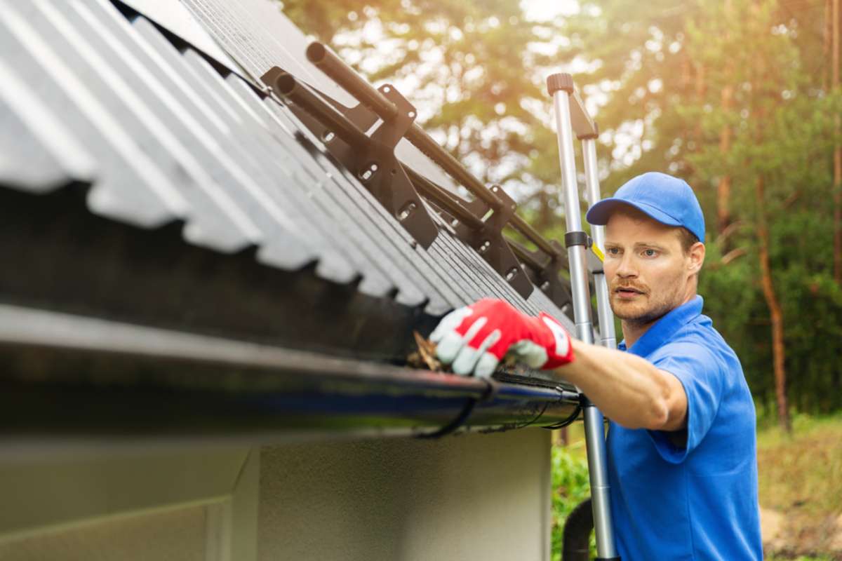 worker cleaning house gutter from leaves and dirt